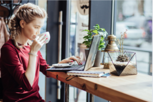 woman-sitting-at-a-coffee bar counter-looking-at-her-laptop-sipping-coffee